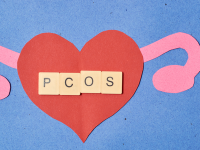 Illustration of PCOS awareness with paper cutouts of a red heart and pink ovaries on a blue background, symbolizing women's reproductive health and hormonal imbalance."