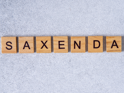 Scrabble-style wooden letter tiles spelling out “Saxenda” on a gray concrete background — referencing the popular weight loss injection featured on andyou.ph.